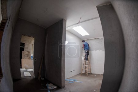 Photo for Construction worker using ladder while plastering on gypsum walls - Royalty Free Image