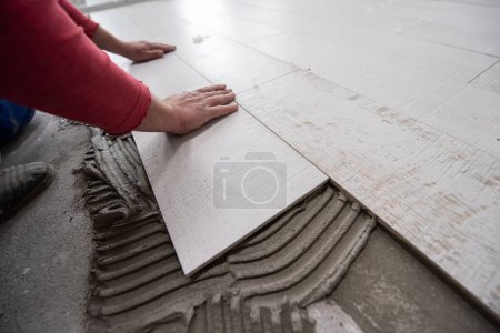 Téléchargez les photos : "travailleur installant les carreaux de céramique effet bois sur le sol" - en image libre de droit