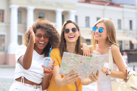 "Foto von drei Mädchen genießen Sightseeing im Freien. Schöne Touristinnen erkunden Stadt mit Karte."