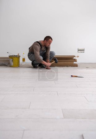Téléchargez les photos : "travailleur installant les carreaux de céramique effet bois sur le sol" - en image libre de droit
