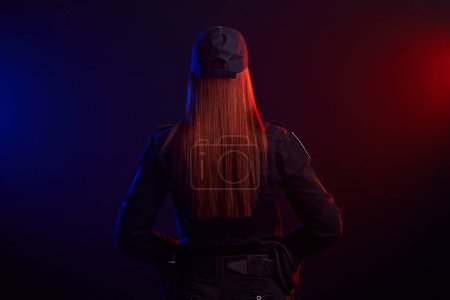 Foto de Mujer policía seria posando para la cámara sobre un fondo negro con retroiluminación roja y azul
. - Imagen libre de derechos
