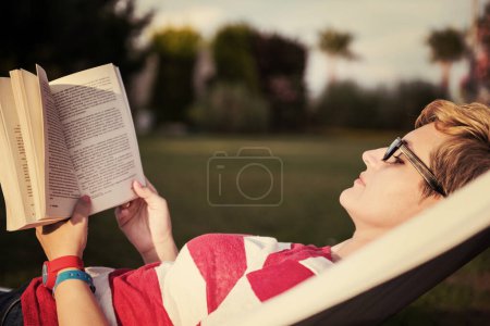 Photo for Woman reading a book while relaxing on hammock - Royalty Free Image