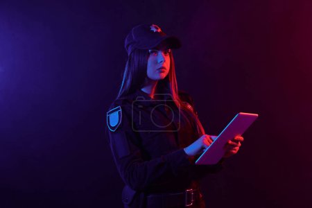 Foto de Retrato de cerca de una agente de policía posando para la cámara sobre un fondo negro con retroiluminación roja y azul
. - Imagen libre de derechos