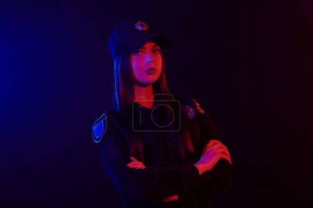 Téléchargez les photos : Portrait en gros plan d'une policière posant pour la caméra sur un fond noir avec rétroéclairage rouge et bleu
. - en image libre de droit