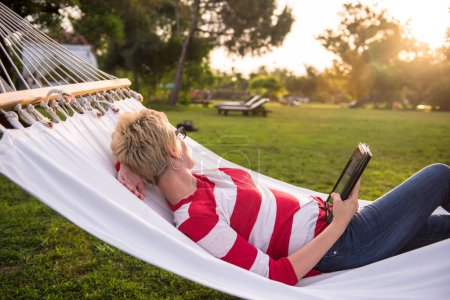 Photo for Woman using a tablet computer while relaxing on hammock - Royalty Free Image