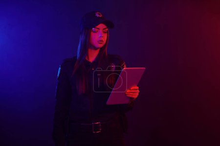 Téléchargez les photos : Une policière sérieuse pose pour la caméra sur un fond noir avec un rétroéclairage rouge et bleu
. - en image libre de droit