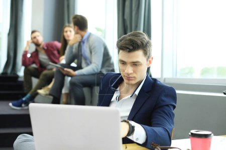 Foto de "Los jóvenes inteligentes están utilizando gadgets mientras trabajan duro en la oficina moderna. Joven trabajando en su portátil
." - Imagen libre de derechos
