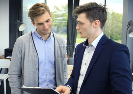 Foto de Dos jóvenes hombres modernos discutiendo el trabajo en la oficina. - Imagen libre de derechos