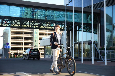 Foto de Joven empresario seguro paseando en bicicleta por la calle de la ciudad - Imagen libre de derechos