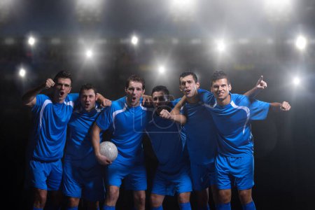 Foto de Futbolistas celebrando la victoria frente al gran estadio moderno con bengalas y luces - Imagen libre de derechos