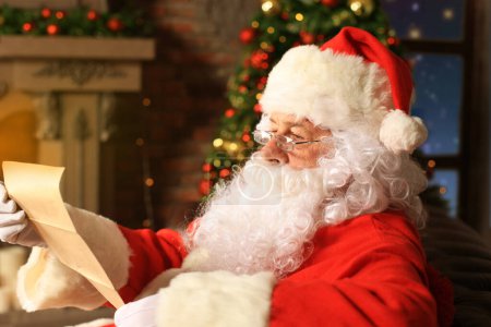 Foto de Retrato de Papá Noel feliz sentado en su habitación en casa cerca del árbol de Navidad y leyendo la carta de Navidad o la lista de deseos. - Imagen libre de derechos