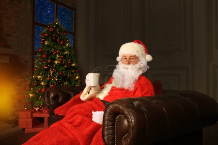 Téléchargez les photos : Père Noël se reposer dans une chaise confortable près de la cheminée à la maison. - en image libre de droit