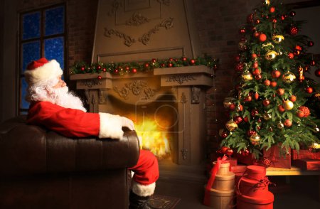 Foto de Santa Claus descansando en una silla cómoda cerca de la chimenea en casa. - Imagen libre de derechos