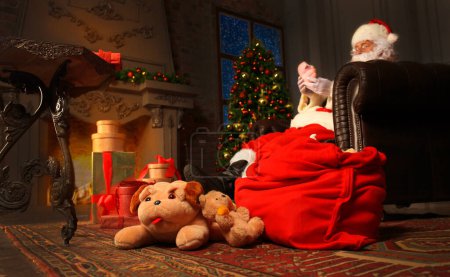 Téléchargez les photos : Portrait du Père Noël heureux assis dans sa chambre à la maison près de l'arbre de Noël et lisant la lettre de Noël ou la liste de souhaits. - en image libre de droit