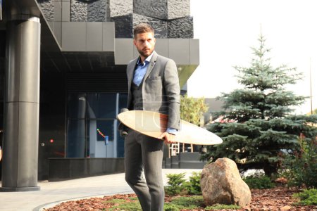 Téléchargez les photos : Jeune homme d'affaires confiant marchant dans la rue, utilisant le longboard - en image libre de droit