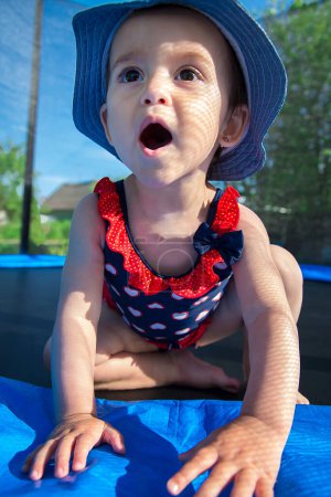 Photo for One and a half year old child in a dress and in Panama is afraid to jump on a trampoline - Royalty Free Image