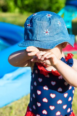 Foto de La niña se cubrió los ojos con las manos cerca de la piscina inflable azul - Imagen libre de derechos