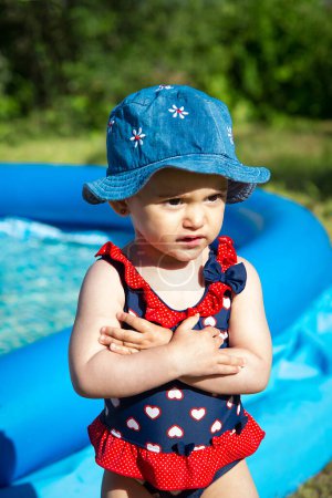 Téléchargez les photos : Une petite fille se tient près de la piscine bleue gonflable - en image libre de droit