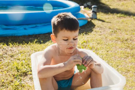 Téléchargez les photos : Un garçon d'âge préscolaire lors d'une chaude journée d'été jouant dans un bain blanc - en image libre de droit