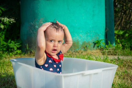 Foto de En un caluroso día de verano, una niña de año y medio se lava la cabeza sola. - Imagen libre de derechos