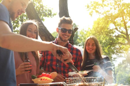 Photo for Happy friends grilling meat and enjoying barbecue party outdoors. - Royalty Free Image