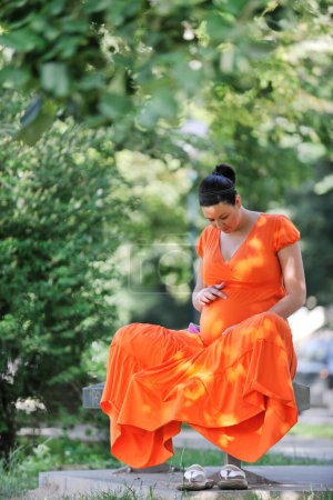 Photo for Pregnant woman in an orange dress posing outdoors, happy pregnancy - Royalty Free Image