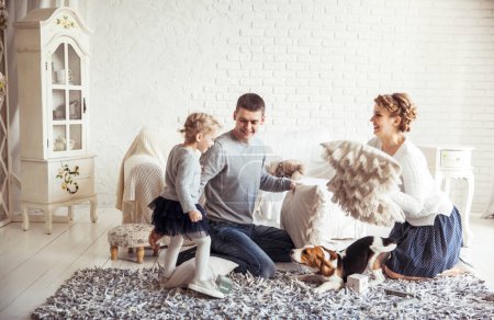 Téléchargez les photos : Famille heureuse et chien de compagnie jouant avec des oreillers dans le salon spacieux - en image libre de droit