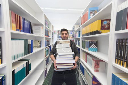 Foto de Estudiante sosteniendo muchos libros en la biblioteca de la escuela - Imagen libre de derechos