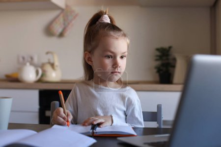 Téléchargez les photos : Sérieux petite fille écriture étude en ligne à l'aide d'un ordinateur portable à la maison, mignon heureux petit enfant prendre Internet leçon web ou classe sur PC. - en image libre de droit