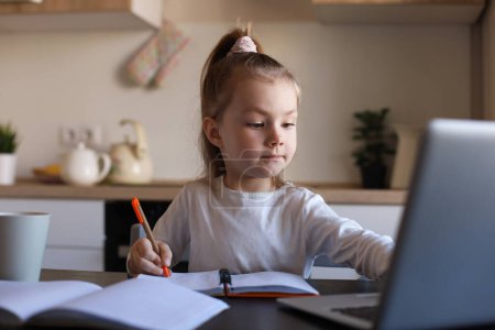 Photo for Serious little girl handwrite study online using laptop at home, cute happy small child take Internet web lesson or class on PC. - Royalty Free Image
