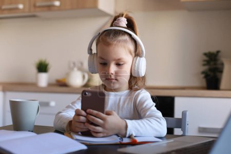 Photo for Smart little girl in headphones do homework online class on smartphone, small child in earphones study on Internet, have web conference or lesson during quarantine. - Royalty Free Image