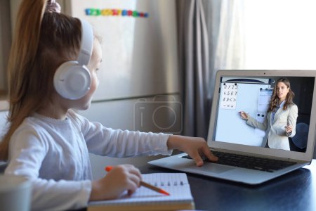Photo for Smart small preschooler girl in headphones watch online lesson and communicate with teacher at home, little child in earphones study on Internet using laptop wireless connection. - Royalty Free Image