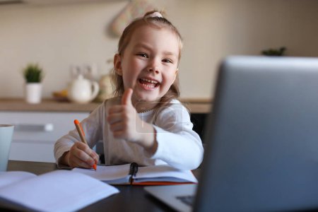 Foto de Niña feliz alumno estudio en línea utilizando el ordenador portátil en casa, sonriendo niño pequeño mostrar pulgar hacia arriba recomiendan clase o lección
. - Imagen libre de derechos