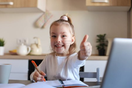 Téléchargez les photos : Happy little girl pupil study online using laptop at home, souriant petit enfant montrer pouce vers le haut recommander classe ou leçon. - en image libre de droit