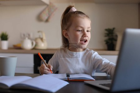 Téléchargez les photos : Souriant petite fille écriture étude en ligne à l'aide d'un ordinateur portable à la maison, mignon heureux petit enfant prendre Internet leçon web ou classe sur PC. - en image libre de droit