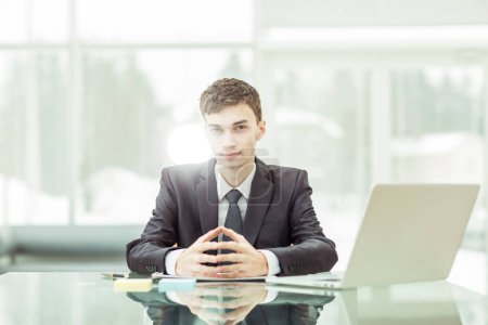 Téléchargez les photos : Jeune homme d'affaires aspirant assis à un bureau devant un ordinateur portable ouvert - en image libre de droit