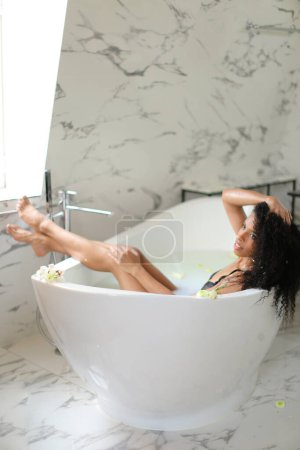 Photo for Young beautiful black girl taking milk bath and wearing swimsuit. - Royalty Free Image