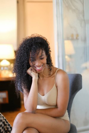 Foto de Joven chica negra feliz sentada en la habitación y con lencería beige. - Imagen libre de derechos