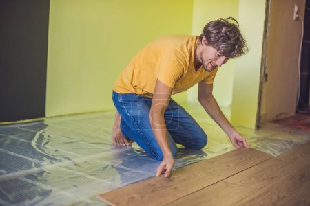 Téléchargez les photos : Homme installant un nouveau plancher stratifié en bois. système de chauffage au sol infrarouge sous plancher stratifié - en image libre de droit