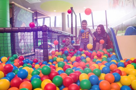 Téléchargez les photos : Jeune maman jouer avec les enfants dans la piscine avec des boules colorées - en image libre de droit