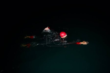 Téléchargez les photos : Athlète de triathlon nageant dans la nuit noire portant une combinaison - en image libre de droit
