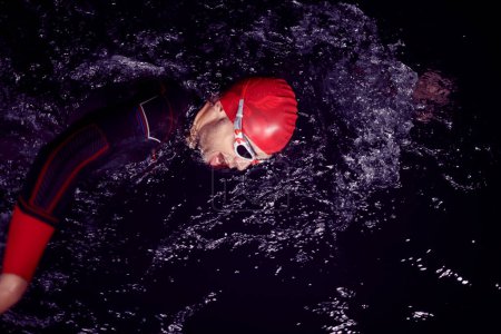 Foto de Atleta de triatlón nadando en la noche oscura usando traje de neopreno - Imagen libre de derechos