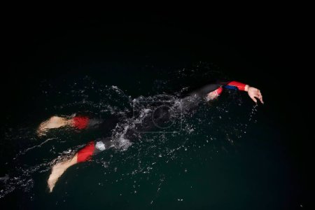 Foto de Atleta de triatlón nadando en la noche oscura usando traje de neopreno - Imagen libre de derechos