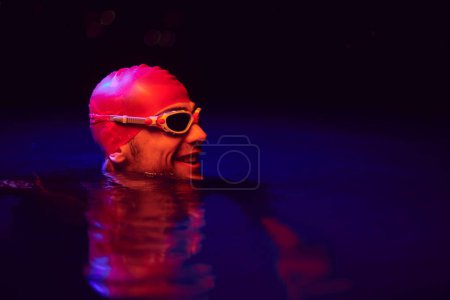 Téléchargez les photos : Authentique nageur triathlète ayant une pause pendant l'entraînement dur sur la lumière de gel de néon de nuit - en image libre de droit