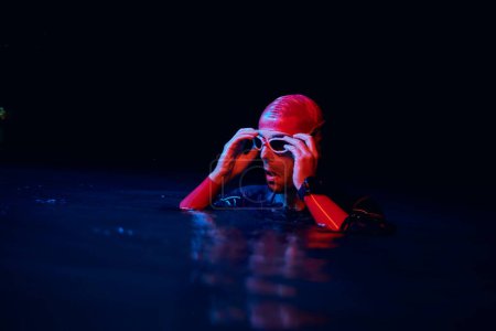 Téléchargez les photos : Authentique nageur triathlète ayant une pause pendant l'entraînement dur sur la lumière de gel de néon de nuit - en image libre de droit