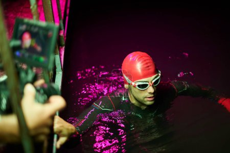 Photo for Videographer  taking action shot of triathlon swimming athlete at night - Royalty Free Image