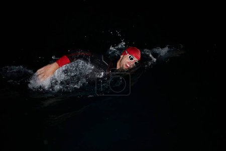 Téléchargez les photos : Athlète de triathlon nageant dans la nuit noire portant une combinaison - en image libre de droit