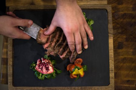 Téléchargez les photos : "vue du dessus des mains du chef servant un steak de boeuf
" - en image libre de droit