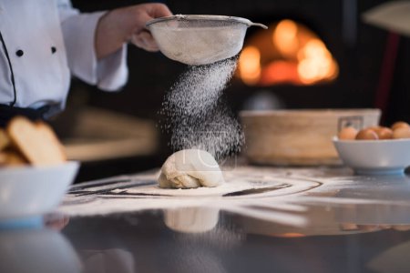 Téléchargez les photos : "chef saupoudrer de farine sur la pâte à pizza fraîche" - en image libre de droit