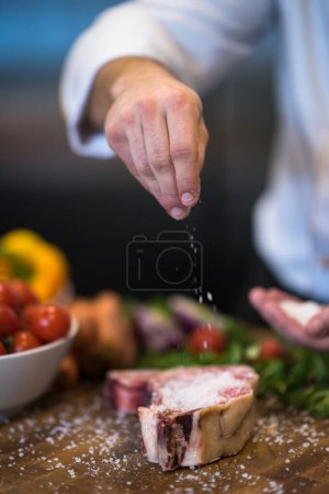 Foto de "Chef poniendo sal en jugosa rebanada de filete crudo
" - Imagen libre de derechos